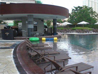 泳池邊浸晌水中嘅籐椅，遠方係poolside bar。