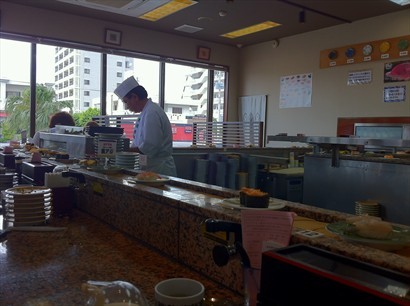 壽司師傅正在認真地準備食物 , 壽司用盤子來計算價錢,  牆壁上掛著盤子和價格。