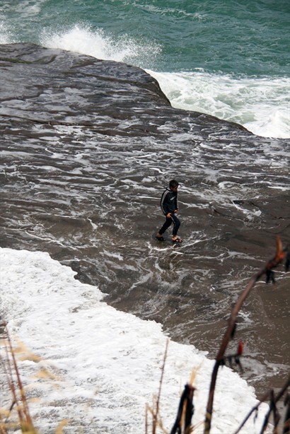 大浪花衝上石上，這位男孩還刻意跑出去，很危險！